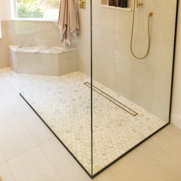Moderne Dusche mit Glasfront, Mosaikfliesen und goldener Brause.